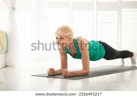 Home training concept. Smiling senior woman doing elbow plank on yoga mat in living room, sporty mature lady doing fitness workout routine, exercising indoors, strengthening her core muscles