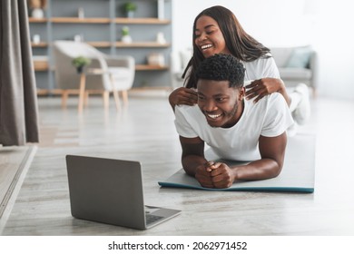 Home Training. Couple Having Fun During Online Workout. Looking At Laptop Screen Watching Virtual Tutorial, Boyfriend Doing Plank Exercise With Girlfriend Lying On Him On His Back In Living Room