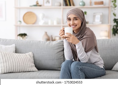 Home Tranquility. Portrait Of Relaxed Muslim Girl In Hijab Sitting On Couch With Coffee, Enjoying Day Off, Copy Space