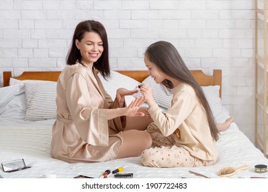 Home Wellness And Spa Day. Cute Teen Girl Making Manicure To Her Beautiful Mother On Bed At Home. Millennial Mom And Her Daughter Painting Nails With Polish, Enjoying Family Times Together