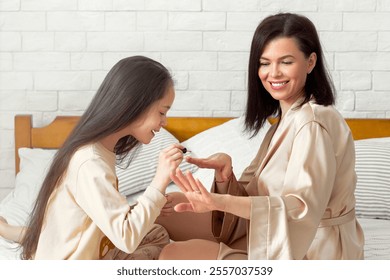 Home wellness and spa day. Cute teen girl making manicure to her beautiful mother on bed at home. Millennial mom and her daughter painting nails with polish, enjoying family times together - Powered by Shutterstock