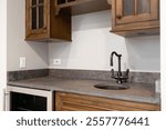 A home wet bar with a bronze faucet on a brown stone countertop, wood cabinets, and a stainless steel wine fridge.