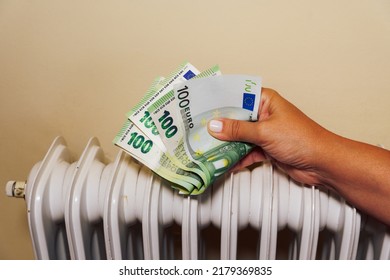 Home Winter Heating Prices Going Up Concept. Female Trying To Get Warm Against A White Radiator, Holding Euro Paper Money.