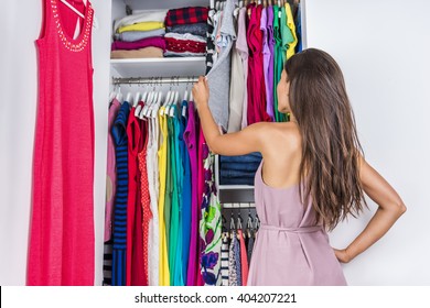 Home Woman Choosing Her Fashion Outfit In Dressing Room. Woman In Bedroom Walk-in Organized Closet Looking At Clothes Hanging Deciding What Shirt To Wear In The Morning. Shopping Store Clothing Rack.