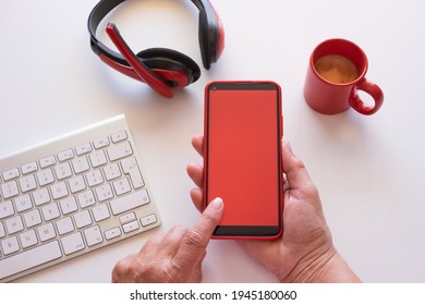 Home worker have a break with coffee cup, using phone with red screen. White desktop and red headphones
