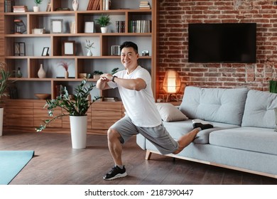 Home Workout Concept. Excited Asian Mature Man Doing Single Leg Split Lunge Near Sofa, Exercising At Home And Smiling At Camera. Domestic Male Fitness And Sporty Lifestyle