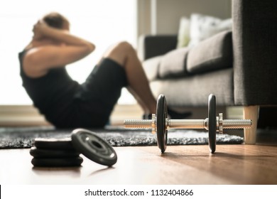 Home workout. Man doing ab training and crunches in living room gym. Guy doing sit ups. Warm up before weight exercise. Fitness concept with dumbbell and athlete.