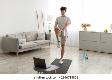 Home Workout Routine. Focused Fit Asian Guy Lifting Leg Up To Chest Stretching Hamstring Muscles, Doing Standing Knee-To-Chest Exercise, Using Pc In Living Room Indoors. Healthy Lifestyle Concept - Powered by Shutterstock