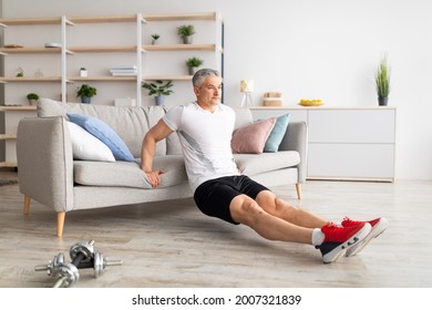 At home workout routine. Sporty mature man leaning on sofa and doing push-up exercises, working out in living room interior, free space. Home training to keep fit