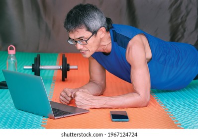 Home workout. Senior man doing yoga plank while watching online class on laptop in living room. Exercising in living room. - Powered by Shutterstock