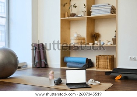 Home workout space featuring exercise mat, dumbbells, laptop, and yoga ball neatly arranged