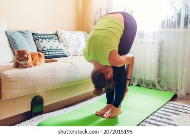 Home yoga workout during coronavirus lockdown. Uttanasana standing forward bend pose. Woman training using mat by cat. Stretching exercises