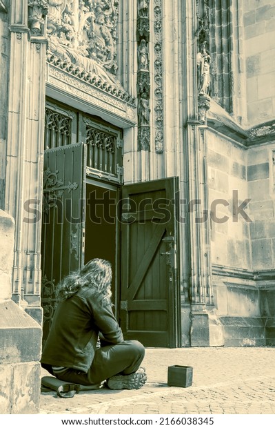 Homeless adult beggar man sitting outdoors in\
front of the church, in city asking for money donation. Begging for\
help and money. Problems of big modern cities. Indifference of\
people. Social issues.