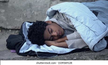 Homeless African Teenager Lying In Sleeping Bag Ground, Poverty Unemployment