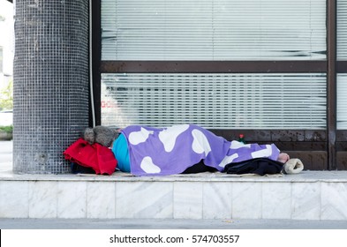 Homeless barefooted woman sleep on the urban street in the city on the sidewalk near the building