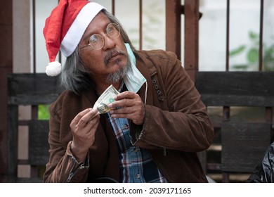 Homeless beggar wears Santa hat and medical mask holding a dollar banknote in Christmas time, looking at the donor
