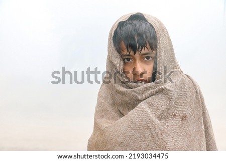 a homeless child is covering his body and face by a warm shawl in extreme cold weather 