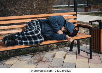 homeless dirty elderly old Caucasian man lies sleeping on a park bench in autumn