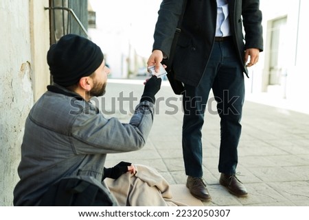 Homeless man with a beard struggling living on the street and receiving money for food from a kind man