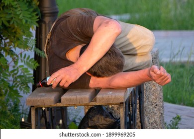 Homeless man fallen down on the ground next to a bench in the park, experiencing lethargy after excessive drinking