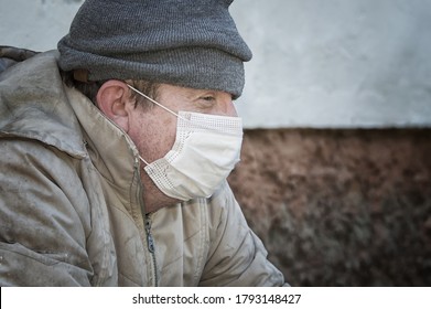 Homeless. A man in ragged clothes and a medical mask is begging. COVID-19. Close up.