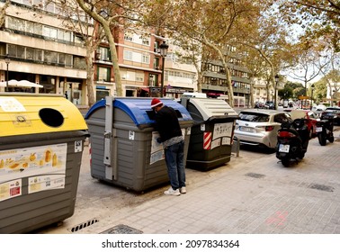 A homeless man in a red Christmas hat searches for food in a dumpster. A beggar man in a hat of Santa Claus climbs in trash containers. December 27, 2021, Spain, Valencia.