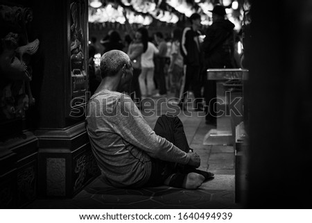 A homeless man sitting at the front of a temple court, there are people strolling in Lantern Festival.