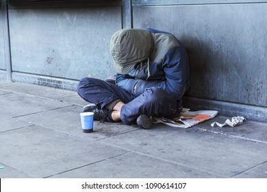 Homeless Man Sitting On The Street In The Shadow Of The Building And Begging For Help And Money. Problems Of Big Modern Cities.