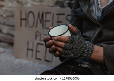 Homeless Man Sitting On The Street In The Shadow Of The Building And Begging For Help And Money. Problems Of Big Modern Cities. Close Up.