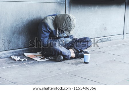 Homeless man sitting on the street in the shadow of the building and begging for help and money. Problems of big modern cities.