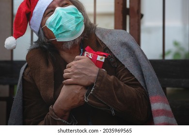 Homeless man wears medical mask and Santa hat closes his eyes and happily hugs his Christmas present