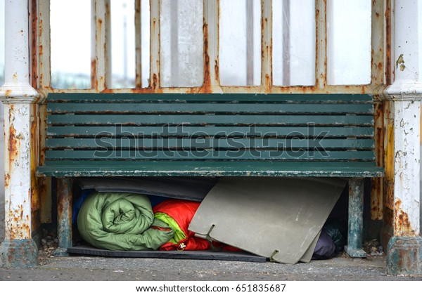 Homeless\
person\'s sleeping bags and bedding under a\
bench