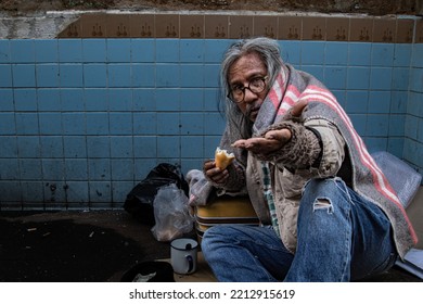 Homeless Poverty Old Man Sitting Reaching Out To Passerby Ask For Money And Eating Bread Waiting For Help. Homeless People Who Do Not Have Home To Sleep On Streets. Donate And Charity Concept.