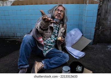 Homeless Poverty Old Man Sitting Reaching Out To Passerby Ask For Money And Eating Bread Waiting For Help. Homeless People Who Do Not Have Home To Sleep On Streets. Donate And Charity Concept.