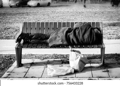 Homeless Refugee Man In Black Coat Sleeps On The Bench On The Street Black And White