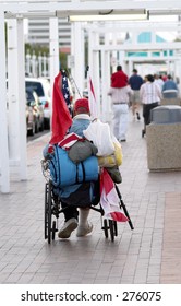 A homeless veteran in a wheelchair, with the American flag and his belongings strapped to the back of the chair.