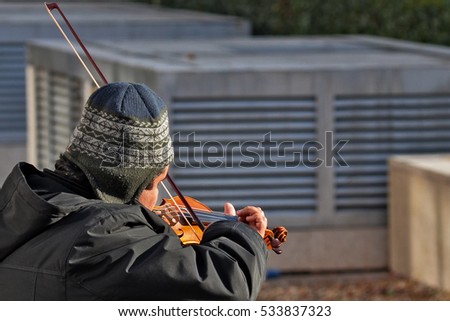 homeless violonist plays on the street on a sunny winter say