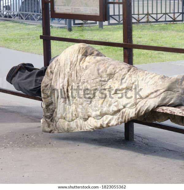 Homeless woman sleeping under a\
blanket at a public transport stop - Moscow, Russia, August 15,\
2020