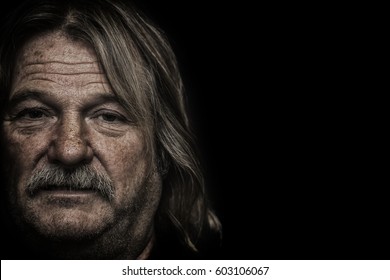 Homelessness. Face Of An Alcoholic Traveler, Hillbilly, Gypsy Or Vagrant. Portrait With Copy Space. Weathered Facial Features Of A Middle-aged To Elderly Man Against Black Background.