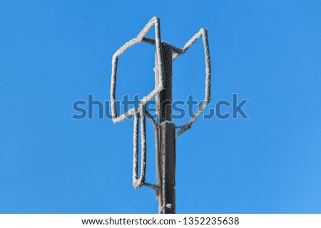 A homemade antenna in the form of a rectangular screen of aluminum wire is tied to a wooden pole against a blue sky on a winter frosty day.