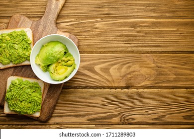 Homemade Avocado Toasts And Smashed Fresh Ripe Avocados In Bowl On Cutting Board On Wooden Rustic Brown Background. Avocado Smash Sandwiches, Healthy Snack For Diet, Clean Eating. Top View, Copy Space