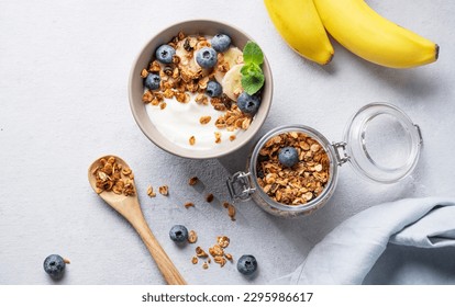 Homemade baked granola with yogurt, blueberries and banana in a bowl on a light background with fresh berries. Healthy vegetarian breakfast with muesli. Top view and copy space. - Powered by Shutterstock