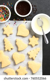 Homemade Baked Sugar Cookies For Christmas With Icing And Sprinkles On The Side, Photographed Overhead On Slate