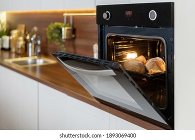 Homemade baking. Open door at electric oven with air ventilation and tray full of whole fresh loaf. Side view of modern technology appliance against kitchen furniture on copy space background - Shutterstock ID 1893069400