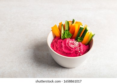 Homemade Beetroot Hummus made from Chickpeas and Beetroot in White Bowl with Carrot and Cucumber Sticks, light grey background. Healthy Vegetarian Detox Snack