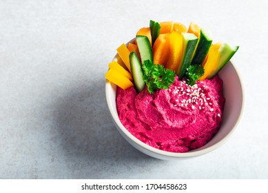 Homemade Beetroot Hummus made from Chickpeas and Beetroot in White Bowl with Carrot and Cucumber Sticks, light grey background. Healthy Vegetarian Detox Snack