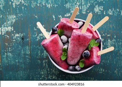 Homemade blueberry ice cream or popsicles decorated green mint leaves on teal rustic table, frozen fruit juice, vintage style, top view - Powered by Shutterstock