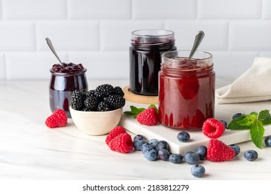 Homemade blueberry, raspberry and blackberry jam in glass jar at white table. - Shutterstock ID 2183812279