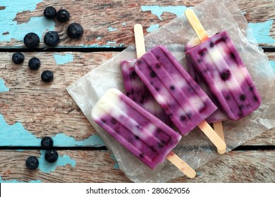 Homemade blueberry vanilla ice pops in a cluster on paper with rustic wood background