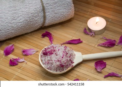 homemade body scrub from sea salt and rose petals and peony candle,pink towel on a straw Mat. Spa concept